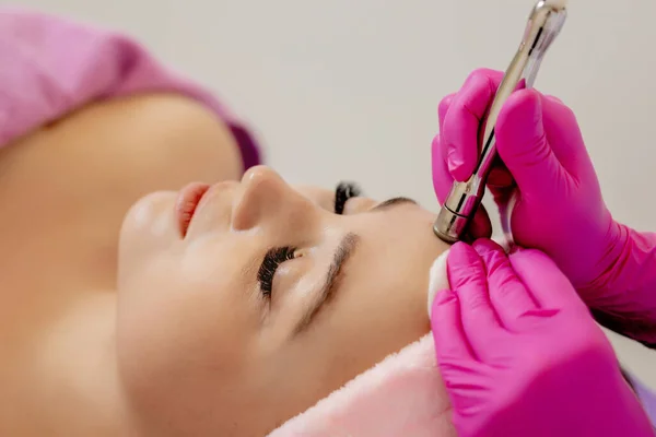 Donanım kozmetolojisi. Kozmetik uzmanı ultrasonik yüz temizleme ameliyatı yapıyor. Genç bir kadın güzellik salonunda ultrasonik soyuluyor. Kozmetik kliniği. Sağlık, klinik, kozmetoloji.