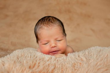 Yeni doğmuş bebek uyuyor, kendi elleriyle ve dirsekleriyle dinleniyor, kahverengi arka planda..