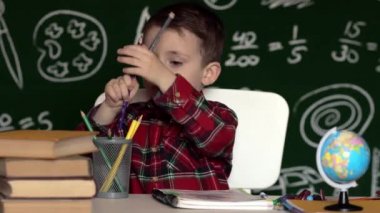 Anaokulu çocuğu okul ödevi yapıyor. Okul malzemeleriyle masasının yanında gülen surat ifadesi olan okul çocuğu. Eğitim. Önce eğitim. Okul kavramı