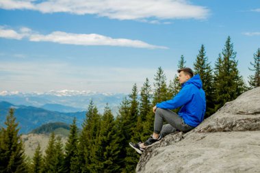 Bir turist uçurumun kenarına oturur ve uzaklara bakar. Otursana. Harika bir dağ manzarası. Yaz, zamandır..