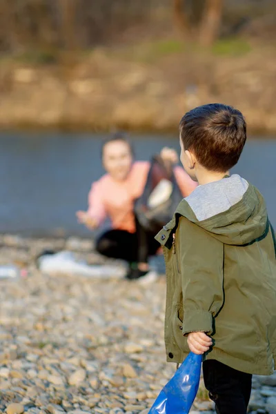 息子と一緒に若い女性は川のゴミ袋にプラスチックごみを収集します 空の使用汚れたプラスチックボトル 環境汚染海岸 — ストック写真