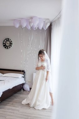 İpek bornozlu genç kadın gelinliğine dokunuyor ve pencerenin yanında dururken gülümsüyor. Düğün günü. Güzellik, moda. En mutlu düğün günü. Her anın tadını çıkar