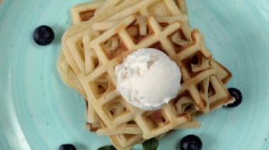 Sunum taze pişmiş klasik Belçika waffleları üzerine dondurma, taze yaban mersini ve ahşap arka planda nane şekeri, tepeden tırnağa manzara. Lezzetli waffle. Kahvaltı konsepti