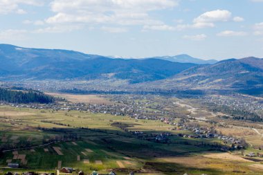 Bulutlu bir yaz gününde Karpat Dağları manzarası. Dağ zirveleri, ormanlar, tarlalar ve çayırlar, güzel doğal manzara.