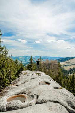 Dağlarda gökyüzüne karşı yükselen bir dağcı zaferi kutluyor, ellerini kaldırıyor..
