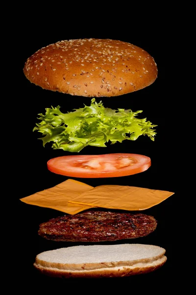 Fliegende Zutaten Burger oder Cheeseburger auf einem kleinen hölzernen Schneidebrett isoliert auf einem dunklen Hintergrund. Burger schwebt in der Luft über dem Tisch. Raum für Text — Stockfoto