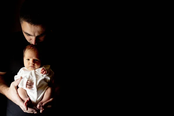 Father holding his 15 days old son in his hand on black background. Baby lying on his father. Holiday concept Father, copy space.
