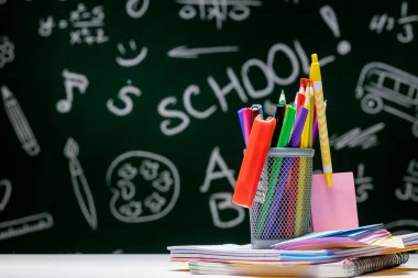 Kırtasiye malzemeleriyle okul geçmişi. Kitap, küre, kalem ve çeşitli ofis malzemeleri yeşil bir karatahta arka planda masanın üzerinde duruyor..