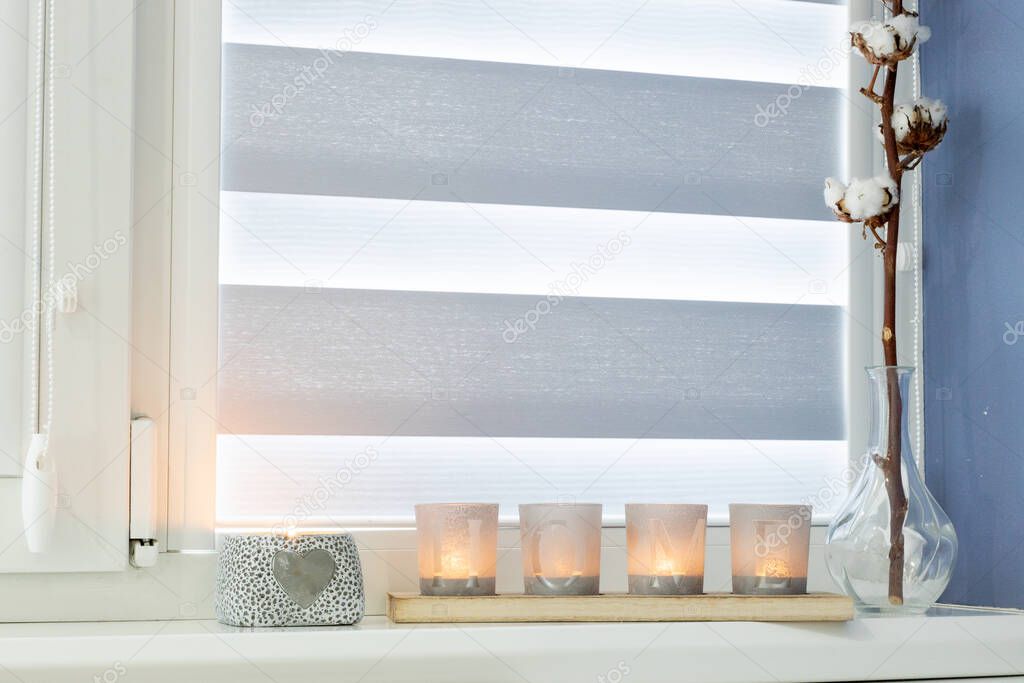 candles with the inscription HOME on the windowsill with beautiful blinds.