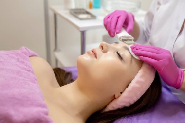 Ultrasonik scrabbing. Genç bir kadın ultrasonda yüz temizleme ameliyatı oluyor. Kozmetoloji yüz bakımı temizliği. Güzellik uzmanı elleri, su jeti ile cildi temizliyor.