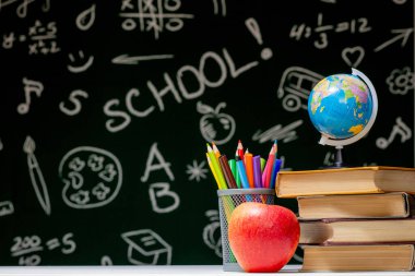 Kitaplar, kalemler ve beyaz masanın üzerindeki elmayla okula geri dön.