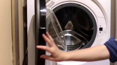 Bir kadın çamaşır yıkar. Bir kadın çamaşır makinesine çamaşır koyar. Ev işleri.
