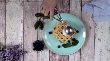 Sunum taze pişmiş klasik Belçika waffleları üzerine dondurma, taze yaban mersini ve ahşap arka planda nane şekeri, tepeden tırnağa manzara. Lezzetli waffle. Kahvaltı konsepti