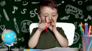 Anaokulu çocuğu okul ödevi yapıyor. Okul malzemeleriyle masasının yanında gülen surat ifadesi olan okul çocuğu. Eğitim. Önce eğitim. Okul kavramı