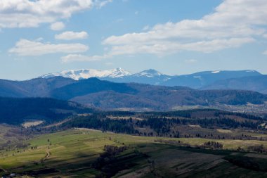 Bulutlu bir yaz gününde Karpat Dağları manzarası. Dağ zirveleri, ormanlar, tarlalar ve çayırlar, güzel doğal manzara..