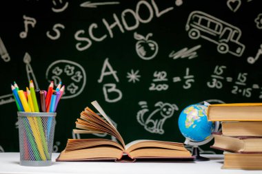 Kitap, kalem ve küre ile okul arka planına yeşil karatahta arka planında beyaz masa üzerinde