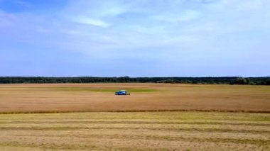 Yazın buğday hasadı. Tarlada çalışan iki hasat işçisi. Hasat makinesini tarlada yetişmiş altın buğday toplamak için birleştirin. Yukarıdan görüntüle