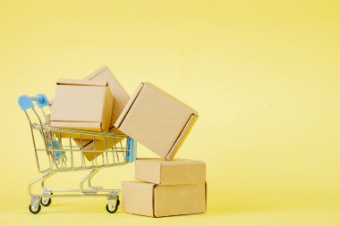 Sarı arka planda alışveriş arabasında kağıt alışveriş torbaları, online alışveriş konsepti