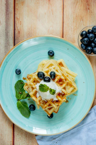 Fresh baked homemade classic Belgian waffles topped with icecream, fresh blueberries and mint on wooden background, top down view. Savory waffles. Breakfast concept — Stock Photo, Image