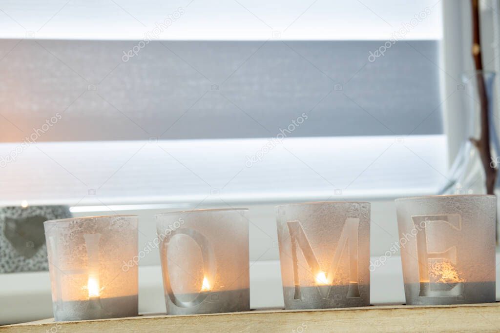 candles with the inscription HOME on the windowsill with beautiful blinds