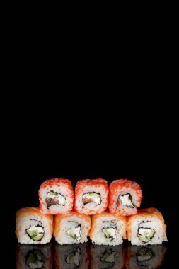 Philadelphia rulosu somon, peynir ve salatalık ile siyah arka planda yansımalı. Suşi Philadelphia.