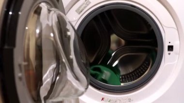 Bir kadın çamaşır yıkar. Bir kadın çamaşır makinesine çamaşır koyar. Ev işleri.