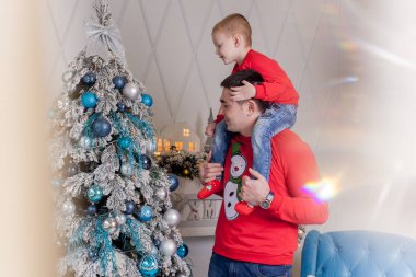 Noel ağacını Noel baloları ve hafif çelenklerle süsleyen mutlu baba ve oğul kış tatillerini kutlamaya hazırlanıyor: Mutlu Noeller ve mutlu yeni yıl 2021. Aile kavramı.