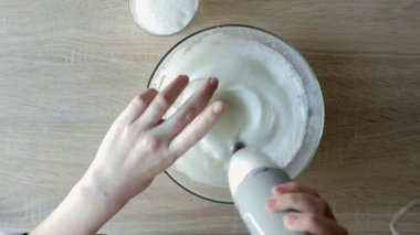 Kadın elleri yumurta beyazı kremlerini çırpıyor. Tahta masadaki karıştırıcıyla. Adım adım Belçika Waffle kurabiyeleri üst görünümü.
