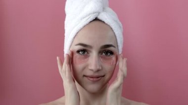 Baş portresi. Göz altı nemlendirici maskeli gülümseyen genç bir kadın. Kameraya bakıp cilt bakımının keyfini çıkarıyor..