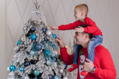 Noel ağacını Noel baloları ve hafif çelenklerle süsleyen mutlu baba ve oğul kış tatillerini kutlamaya hazırlanıyor: Mutlu Noeller ve mutlu yeni yıl 2021. Aile kavramı.