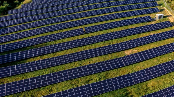 Solar Power Station in Green Field on Sunny day. Aerial view. Solar Panels Stands in a Row in Field for Power Production. Drone fly over Solar Farm. Renewable green energy. Alternative energy sources