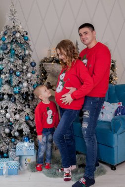 Üç kişilik mutlu bir aile, yeni bir bebek bekleyen genç bir anne, baba ve küçük oğulları Noel ağacının yanında..