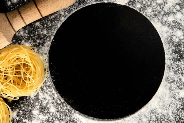Freshly cooked pasta is lying on a dark surface dusted with flour. Italian pasta. Tagliatelle. Raw pasta. Italian pasta recipe. Top view, copy space.