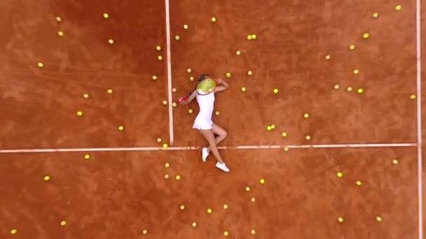 在室外艰苦的网球训练之后 带着很多球和球拍在网球场上放松的微笑女孩的画像 多莉开枪了顶部视图 — 图库视频影像