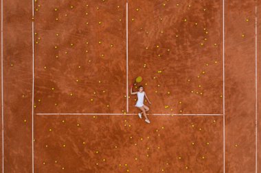 Açık tenis antrenmanından sonra tenis kortunda bir sürü top ve raketle rahatlayan gülümseyen kızın portresi. Dolly vurdu. Üst görünüm