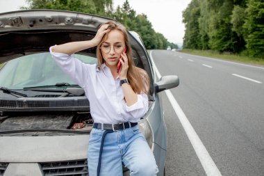 Kaputu patlamış, bozuk bir arabanın yanında duran genç bir kadın aracıyla sorun yaşıyor. Çekici ya da teknik destek bekliyoruz. Bir kadın servis merkezini arıyor..