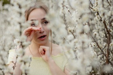 Genç kız sümkürme ve çiçek açan ağacın önünde mendile hapşırma. İnsanları etkileyen mevsimsel alerjik maddeler. Güzel bayanın rhinitis 'i var..