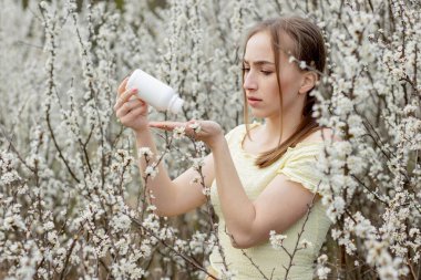 Elinde ilaç olan, bahar alerjileriyle savaşan, mevsimlik çiçeklerle çevrili alerjik bir kadının portresi..