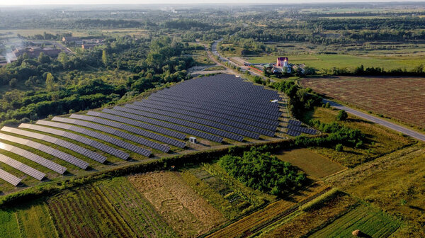 Солнечная электростанция в Зеленом поле в солнечный день. Вид с воздуха. Солнечные панели стоят в ряд в поле для производства электроэнергии. Беспилотник пролетает над Солнечной фермой. Возобновляемая зеленая энергия. Альтернативные источники энергии
