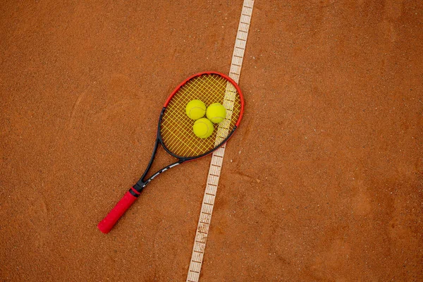 Tennis racket and yellow balls on a brick red court.