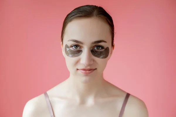 Head shot portrait close up smiling young woman with under eye moisturizing patches mask looking at camera enjoying skincare procedure.