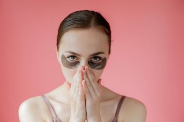 Baş portresi. Göz altı nemlendirici maskeli gülümseyen genç bir kadın. Kameraya bakıp cilt bakımının keyfini çıkarıyor..