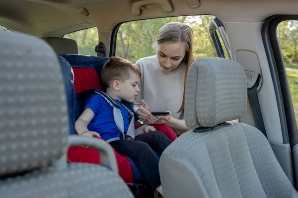 Мама Дает Телефон Маленькому Мальчику Сидящему Автомобильном Кресле Безопасность Перевозки — стоковое фото