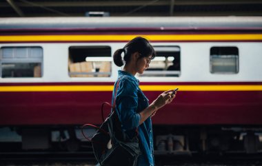 Bekle ve onay zamanlama Tren İstasyonu - platform üzerinde tren iken Asyalı kadın kullanılan gezgin akıllı telefon seyahat ve ulaşım kavramı