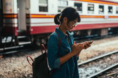 Bekle ve onay zamanlama Tren İstasyonu - platform üzerinde tren iken Asyalı kadın kullanılan gezgin akıllı telefon seyahat ve ulaşım kavramı
