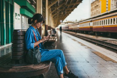 Bekle ve onay zamanlama Tren İstasyonu - platform üzerinde tren iken Asyalı kadın kullanılan gezgin akıllı telefon seyahat ve ulaşım kavramı