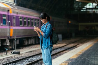 Bekle ve onay zamanlama Tren İstasyonu - platform üzerinde tren iken Asyalı kadın kullanılan gezgin akıllı telefon seyahat ve ulaşım kavramı