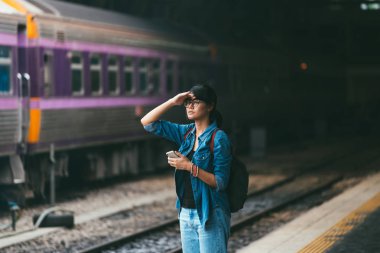 Asyalı kadın kullanılan gezgin akıllı telefon bekleme sırasında ve tren kontrol