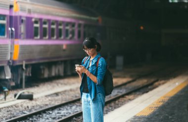 Asyalı kadın kullanılan gezgin akıllı telefon bekleme sırasında ve tren kontrol