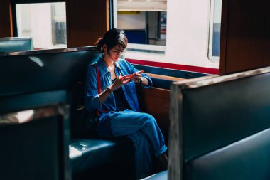 Asyalı kadın gezgin oturur tren koltuk ve kullanılan akıllı telefon bekleme bırakarak Garı tren istasyonuna - süre seyahat ve ulaşım kavramı